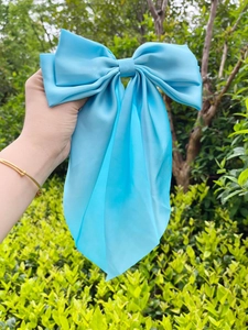 Macro detail of large sky blue satin bow hair clip with glossy texture and metal spring
