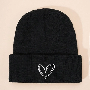 Detailed close-up of white heart embroidery on a black knitted winter beanie hat