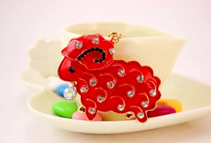 Detail of red enamel sheep keychain with rhinestones resting on a white ceramic cup