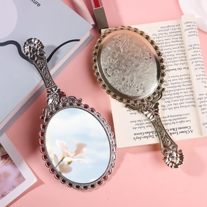 Vintage silver handheld vanity mirror with embossed floral pattern on pink background