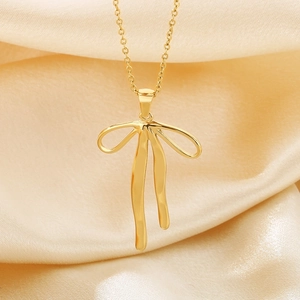 Detailed view of a gold bowknot necklace elegantly placed on soft beige silk fabric