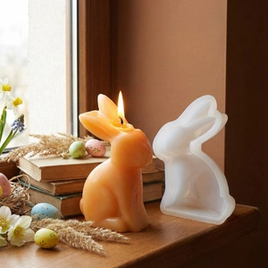 Detail of 3D rabbit silicone mold and a lit orange beeswax candle for Easter DIY crafts