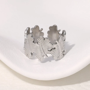 Anillo de acero inoxidable con diseño de hojas sobre un soporte de exhibición blanco
