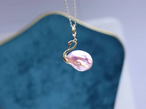 Vue macro du pendentif cygne avec perle baroque rose et détail de pierre précieuse rouge