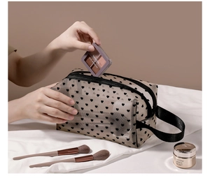 Close-up of black mesh heart makeup bag being filled with cosmetics and brushes