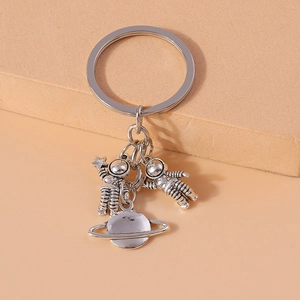 Silver metal astronaut keychain with 3D space planet charms on a minimalist background
