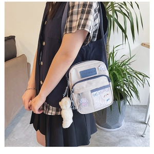 Détail de la bandoulière en nylon crème avec bordure bleue et charmant pendentif ours
