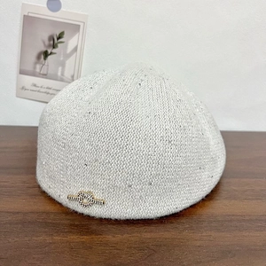 Close-up of a light gray knitted beret featuring sparkling sequins and a crystal heart knot