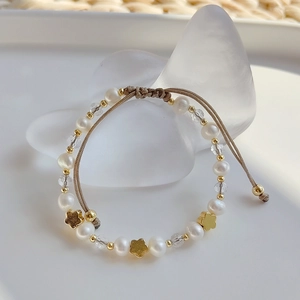 Detailed macro view of woven bracelet with freshwater pearls and gold flower accents