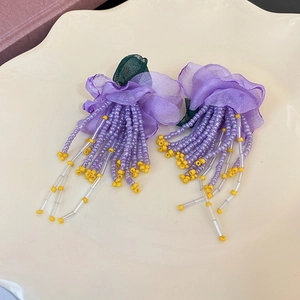 Détail de boucles d'oreilles fleur en mousseline violette avec de longues franges perlées