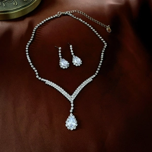 Elegant silver necklace and teardrop earrings set with sparkling crystals on silk background