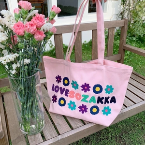 Pink canvas tote bag with floral embroidery and LOVE SOZAKKA text on a park bench