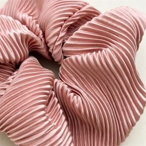 Macro shot of pink pleated satin hair scrunchie showing glossy texture and detail