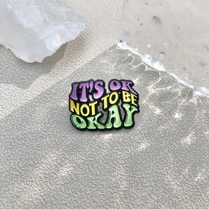 Colorful enamel pin with IT'S OK NOT TO BE OKAY motivational quote on grey background