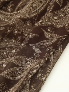 Detailed macro shot of dark brown chiffon fabric with white paisley patterns and soft pleats