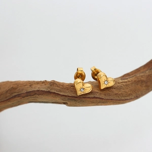 Golden heart earrings with round zircon stones on a rustic wood branch, white background