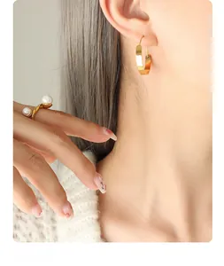 Detailed close-up of golden flat hoop earrings and a minimalist double pearl open ring