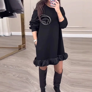 Détail d'une robe noire à manches longues avec rose en strass et ourlet volanté
