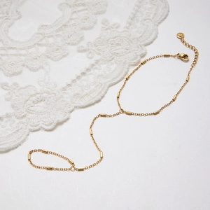 Detail eines minimalistischen goldenen Handketten-Armbands aus Edelstahl mit Spitzenakzent