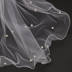 Close-up of white bridal veil featuring hand-beaded pearls and scalloped wavy edges