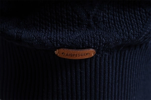 Macro shot of dark blue knit fabric featuring a branded brown leather logo patch detail