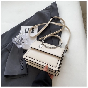 Detail of cream flap bag with black piping, metal chain, and stylish urban props