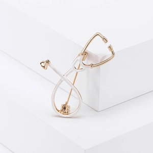 Detailed macro view of a stethoscope brooch pin with gold metal and white enamel finish