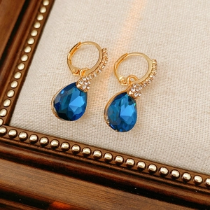 Détail de boucles d'oreilles dorées avec pierres bleues et strass sur tissu beige
