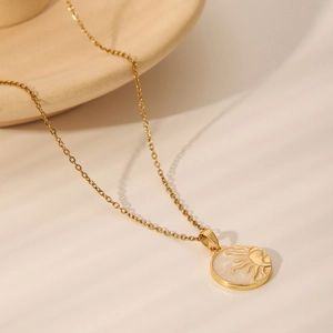 Minimalist gold chain necklace featuring a white sunburst pendant on a ceramic tray
