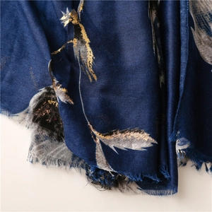 Macro shot of dark blue scarf featuring gold foil feather patterns and soft frayed edges