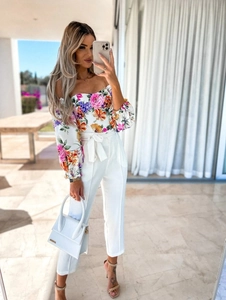 Detailed view of floral off-shoulder top paired with white high-waist belted trousers