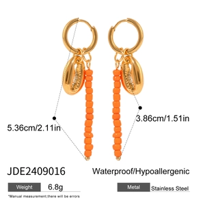 Detail view of gold stainless steel earrings with seashell charms and orange beads