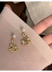 Detailed view of rocking horse pearl earrings with sparkling rhinestones and gold finish