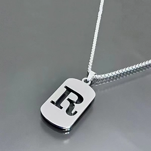 Detail of silver rectangle military tag necklace with cutout letter R on box chain