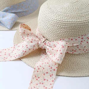 Detail of straw sun hat featuring floral ribbon bow and intricate spiral weave texture