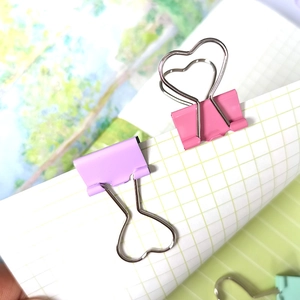 Macro shot of heart-shaped metal binder clips in pastel pink and purple on grid paper