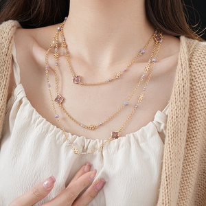 Detail of layered gold necklace with purple beads and square patterned vintage pendants