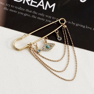 Detail of gold safety pin brooch with multi-layer chains and crystal evil eye charms