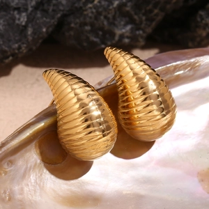 Detailed close-up of gold hollow teardrop earrings with spiral ribbed texture on rock