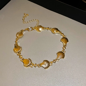 Detail of a gold metallic shell bracelet with linked elements and adjustable lobster clasp