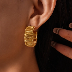 Macro shot of gold geometric C-shaped hoop earrings with intricate grid mesh texture