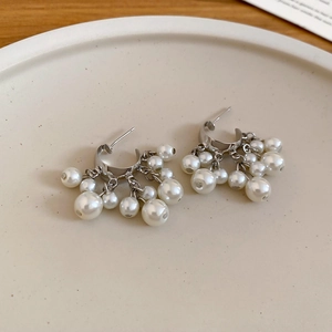 Detail of silver C-shape earrings with cascading pearl clusters on a ceramic tray