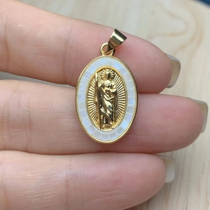 Oval gold Jesus pendant with white shell inlay held by hand to show size and detail