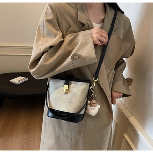Detail of canvas bucket bag with leather trim and sheep charm on a trench coat