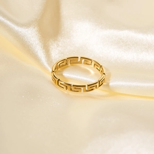 Polished 18K gold stainless steel ring with Greek fret pattern on beige silk fabric