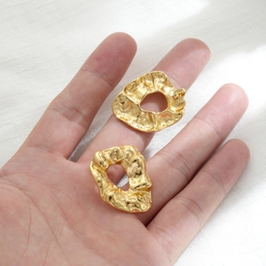 Irregular gold foil textured hoop earrings in stainless steel held in palm for scale