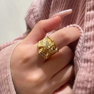 Bague artistique plaquée or aux plis irréguliers portée sur mannequin avec fond chaud