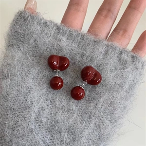 Détail de boucles d'oreilles en résine rouge en forme de cœur sur un pull en mohair gris