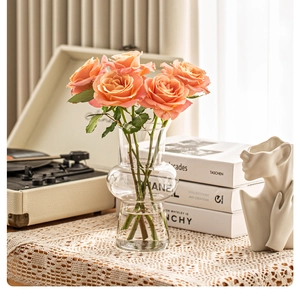 Detailed view of a clear glass vase with pink roses in a stylish vintage living room setting