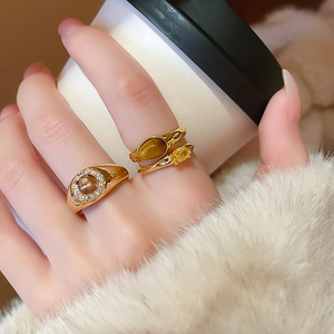 Close-up of gold-plated rings featuring tiger eye stones and cubic zirconia on hand
